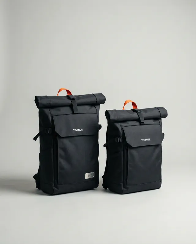 T+3, The Go Bag: two matte black roll-top packs with orange pull tabs and the T-MINUS wordmark, on a pale grey studio floor